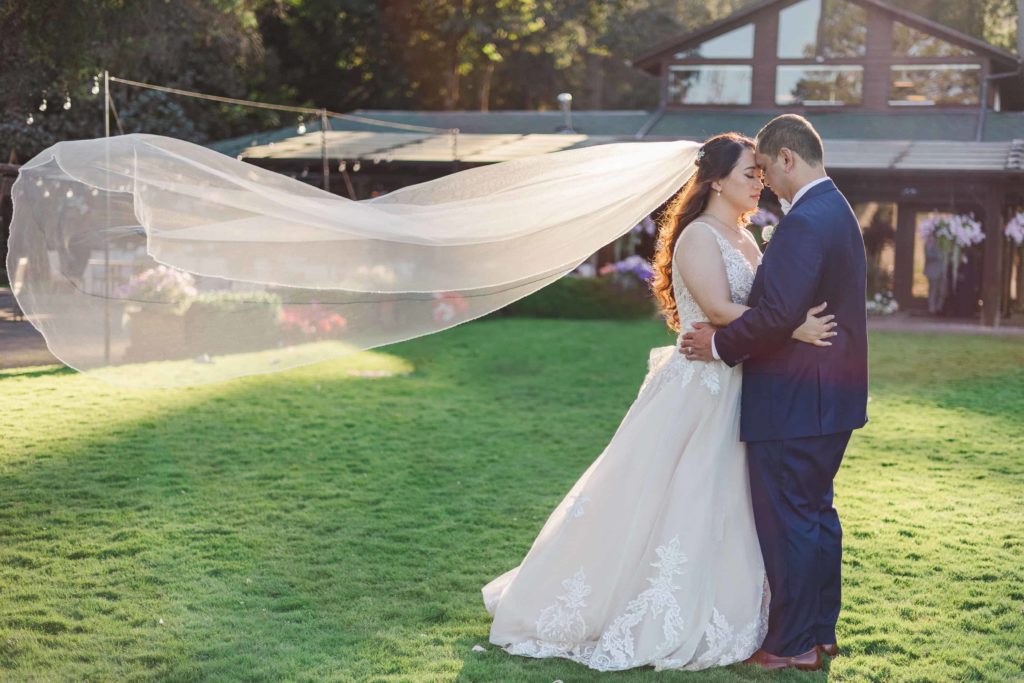 Bride and groom in close embrace, and the brides veil is flowing in the wind